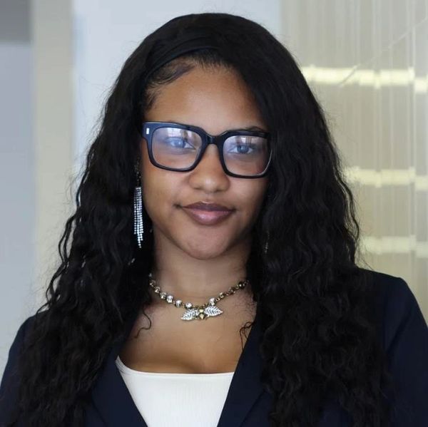 Confident woman with long curly hair, glasses, and stylish jewelry.