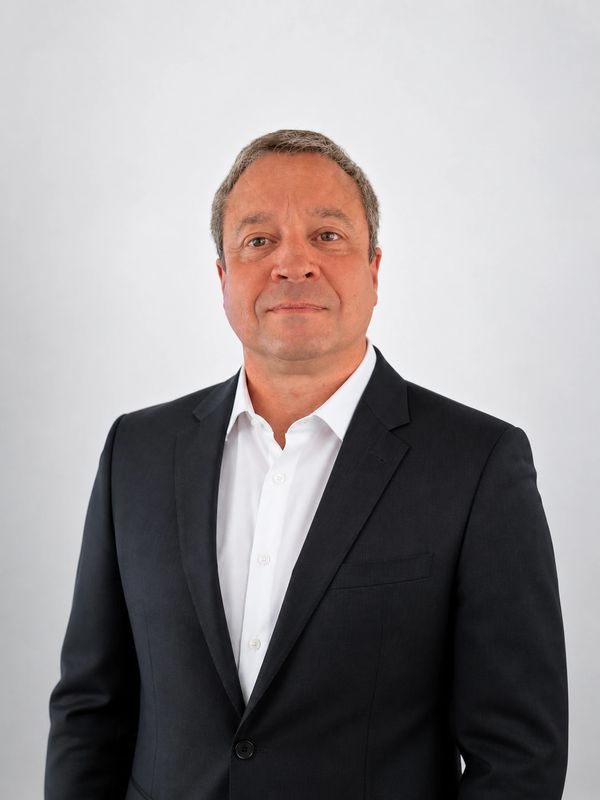 Middle-aged man in a dark suit and white shirt posing against a plain background.