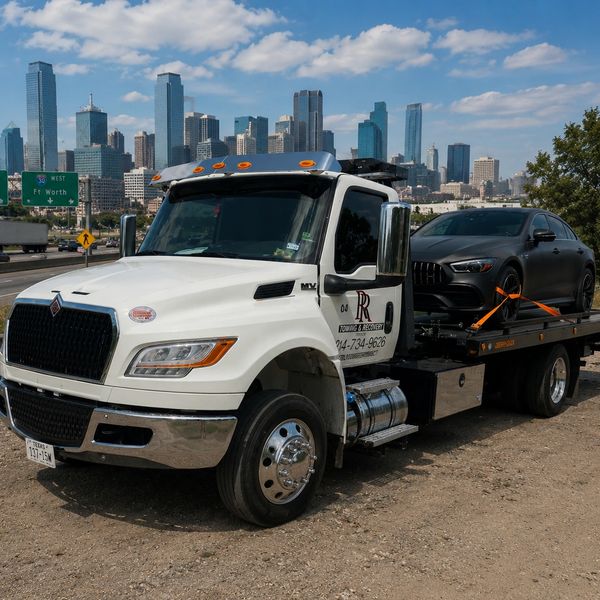 Tow truck carrying a black luxury sports car with city skyline in background.
