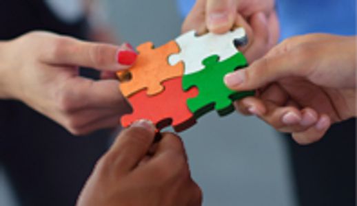 Four hands connect colorful puzzle pieces symbolizing teamwork.