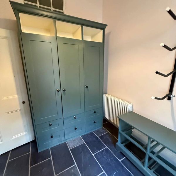 A green wardrobe and shoe rack in a room with black tiled flooring.