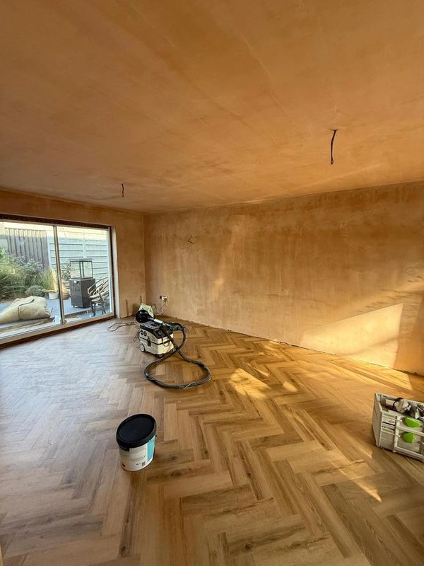 An empty room with freshly plastered walls and wooden herringbone flooring under renovation.