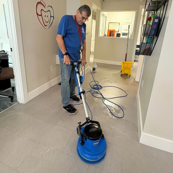 Man using a floor cleaning machine in a dental office corridor.