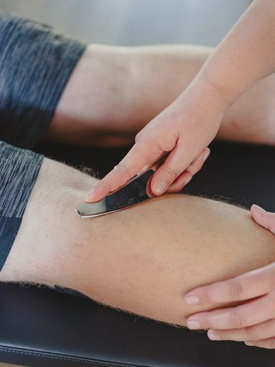 Chiropractor Dr. Kayla Rynne using a metal IASTM tool to treat a patient's calf muscle