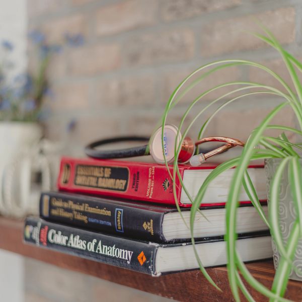 Three anatomy textbooks and a stethoscope lying on a shelf next to a spider plant