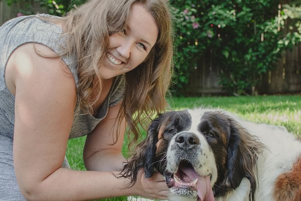 Dr. Kayla Rynne bent over petting her Saint Bernard dog Ellie who is smiling with her tongue hanging