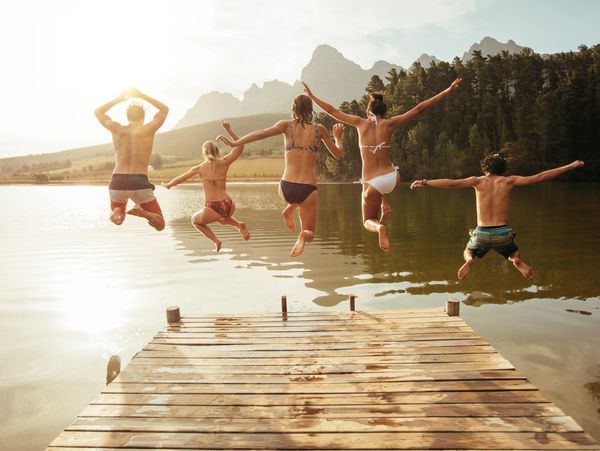 Young friends jumping into lake from a jetty