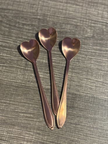 Three copper heart-shaped spoons on a textured surface.