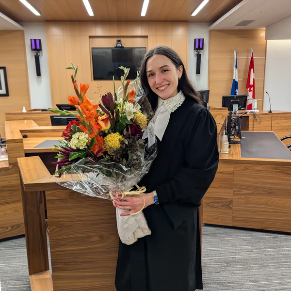 Avocate portant sa toge, son rabat et tenant un gros bouquet de fleurs pour son assermentation