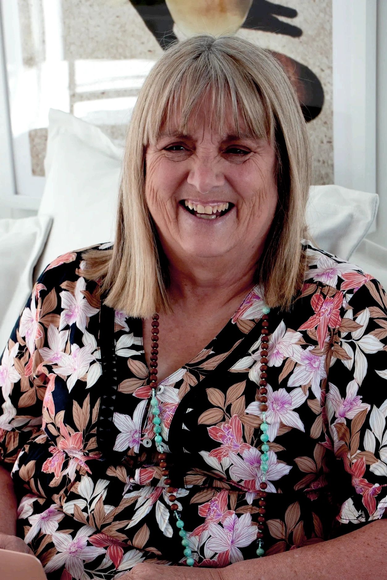 Smiling woman with floral top and beaded necklace.