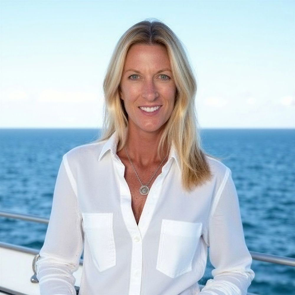 Smiling woman in a white shirt on a boat with the ocean behind her.