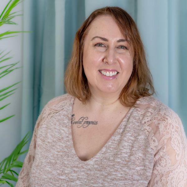 Smiling woman with tattoo and nose ring in cozy lace top.
