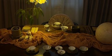 Cozy dimly lit table with tea bowls, a plant, and soft fabric draped across.