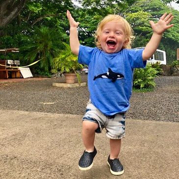 A joyful toddler jumping with arms raised outdoors.