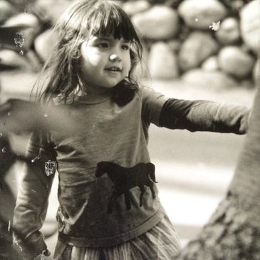 A young girl with a horse print shirt playing outdoors near rocks.