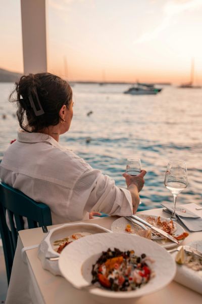 Woman enjoying a relaxed meal overlooking the water at sunset.