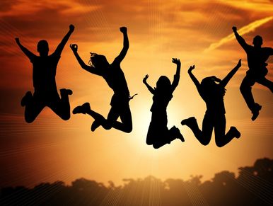 Group of people jumping together outdoors against a sunset sky.