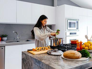 Woman preparing a meal with fresh vegetables and ingredients in a home kitchen.