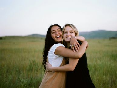 Two women embracing outdoors in a green field.