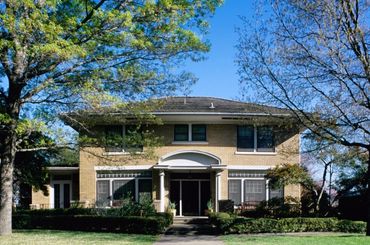 A large two-story brick house with trees and bushes in front.