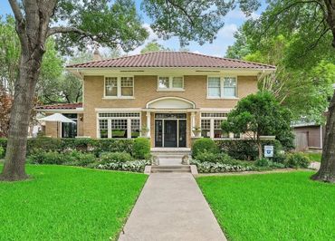 Elegant two-story brick house with a tiled roof and lush green lawn.