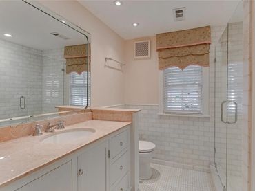 Clean bathroom with marble countertop, glass shower, and decorative window valance.