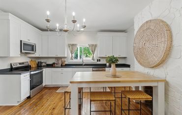 Bright kitchen with white cabinets, wooden floors, and a natural wood dining table.