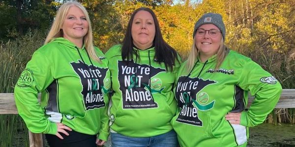 Three women wearing matching green hoodies that say "You're Not Alone."