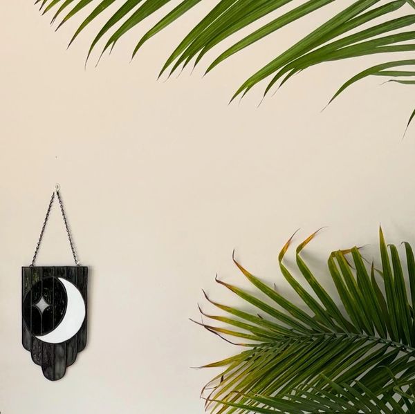 White moon with a white star and scalloped background in black glass, piece is on a wall with leaves