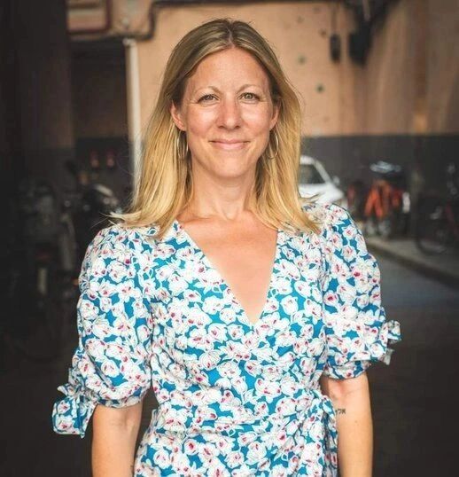 Smiling woman in a floral dress standing indoors with a cozy ambiance.