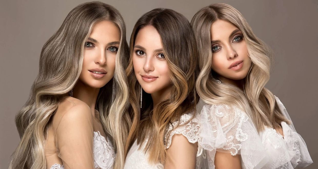 Three women with styled hair and white lace dresses posing together.