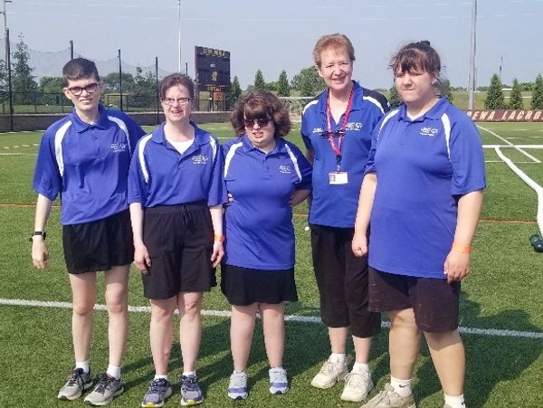 Five people in matching blue shirts standing on a sports field.