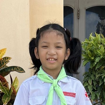 Young girl in school uniform smiling outdoors.