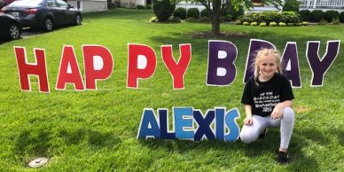 Girl posing next to colorful birthday signs in a green yard.