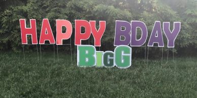 Colorful yard signs spelling Happy BDay Bigg on green grass.