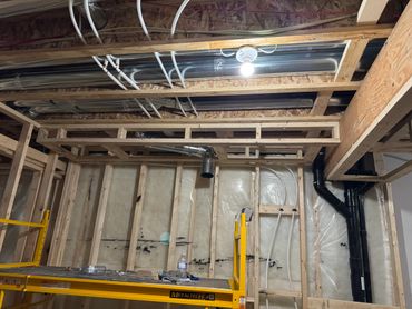 Unfinished basement with exposed wooden framing, pipes, and a work scaffold.