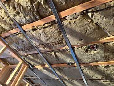 Ceiling insulation with exposed wooden framing and electrical wiring.