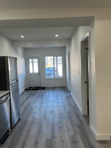 Empty modern kitchen and hallway with gray flooring and white walls.