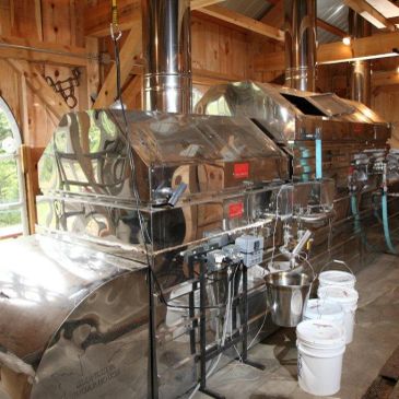 Industrial stainless steel maple syrup evaporator inside a wooden building.