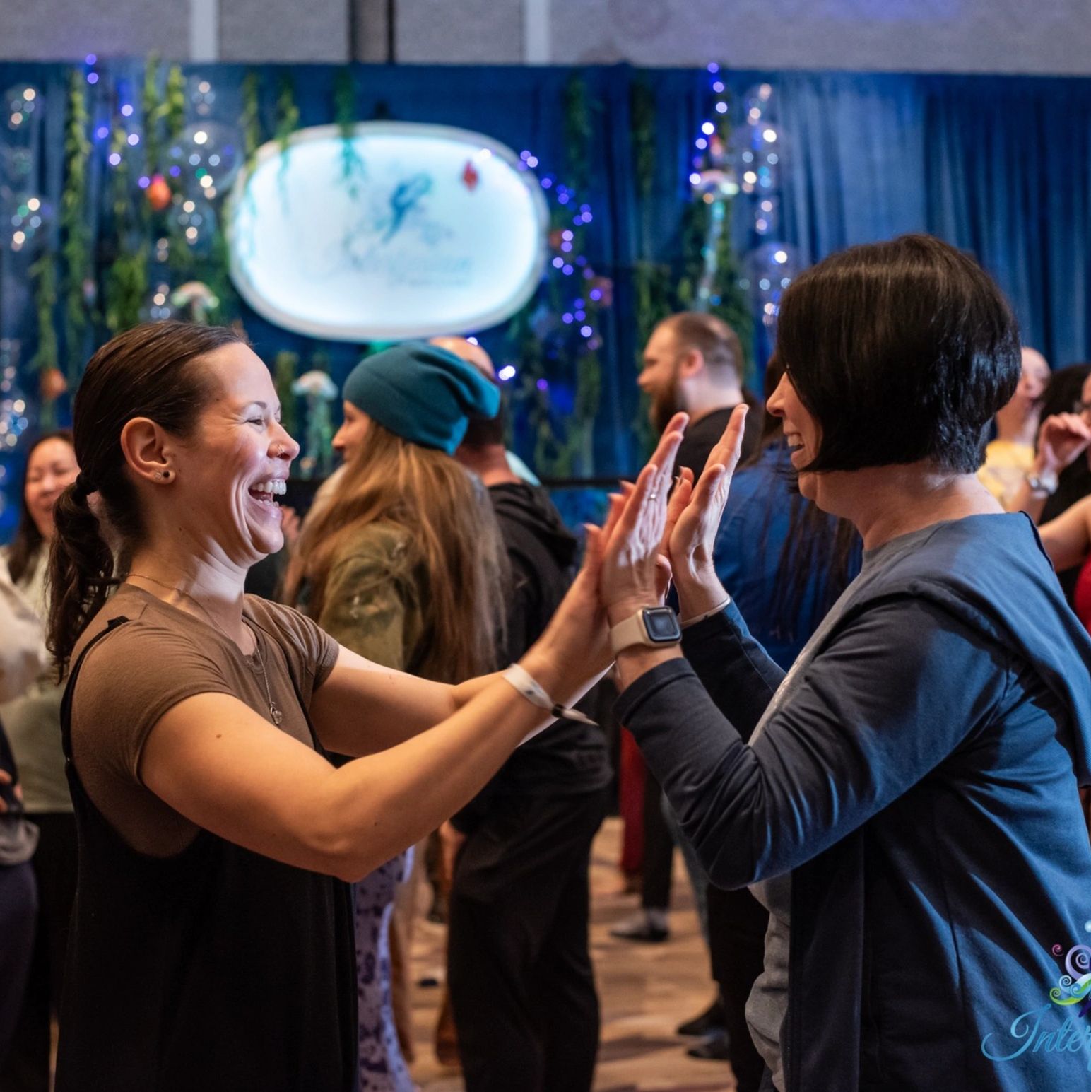 Two women joyfully high-five each other in a lively, decorated indoor event.