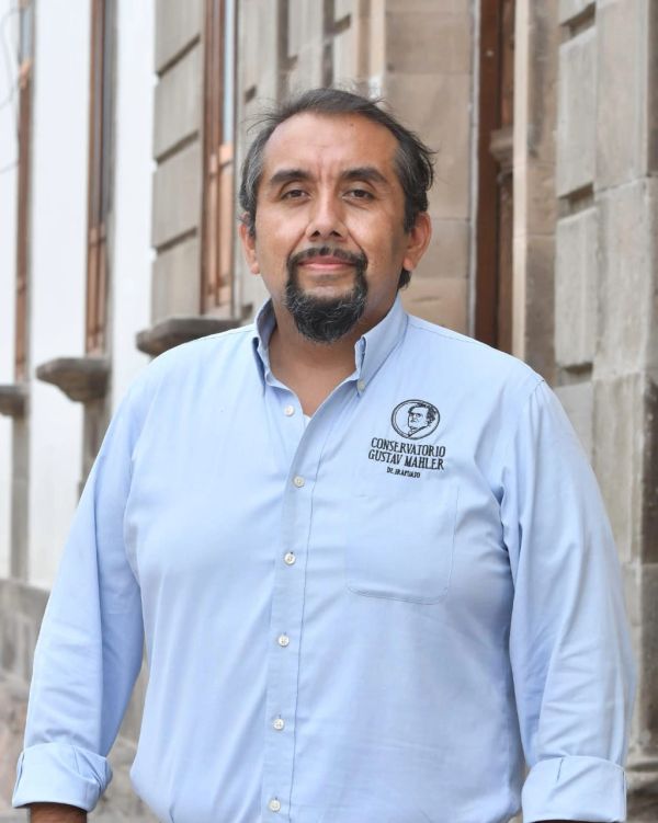 Man in a blue shirt standing outdoors near a stone building.