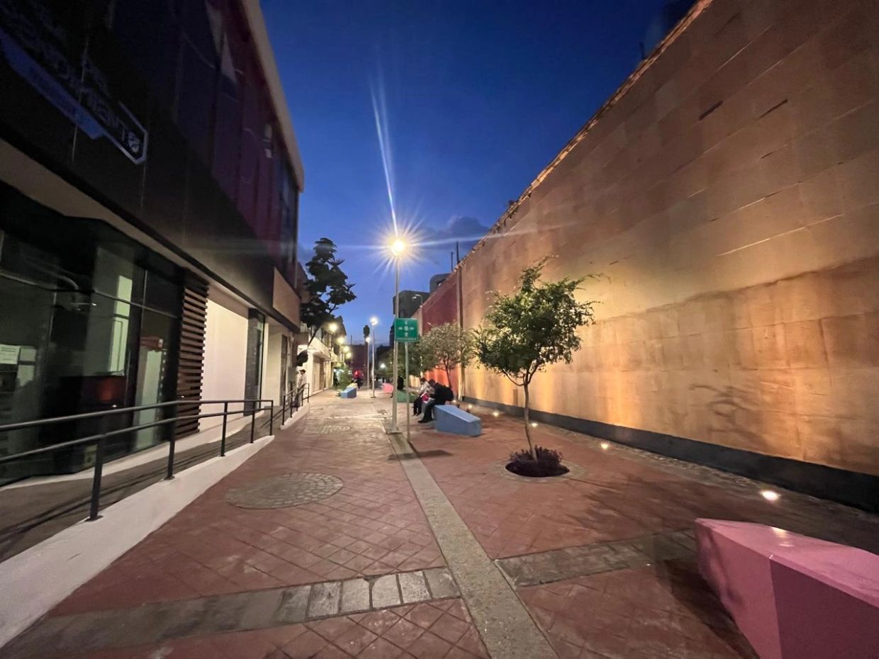 Evening street scene with benches, trees, and warm wall lighting.