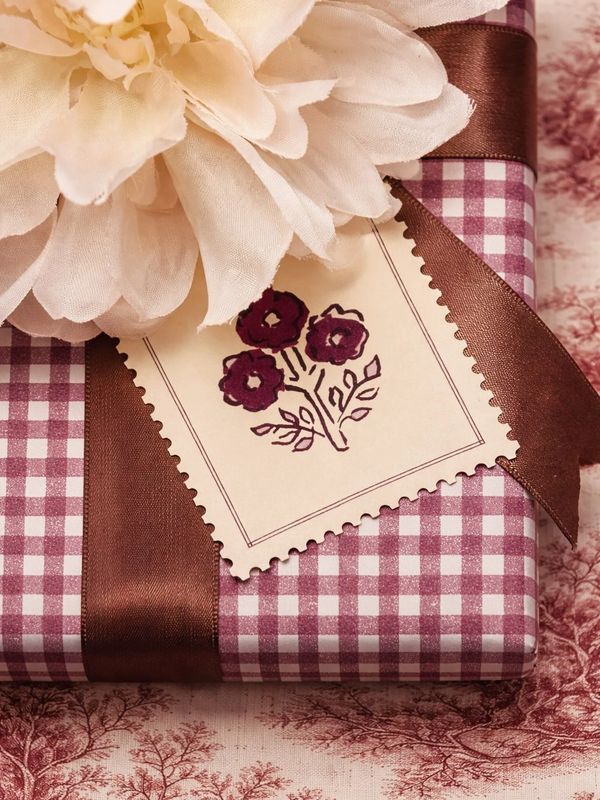 Gift wrapped in checkered paper with brown ribbon and flower tag.