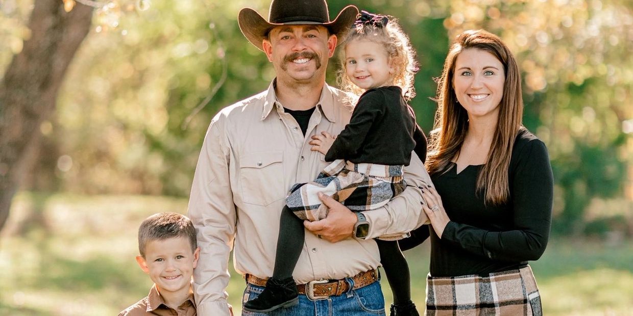 A smiling family of four posing outdoors with autumn colors.
