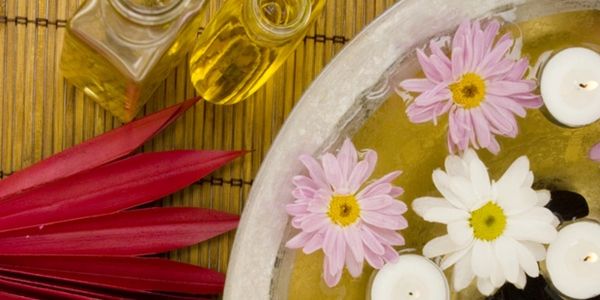 Fragrance massage oil next to flowers and candles floating in water