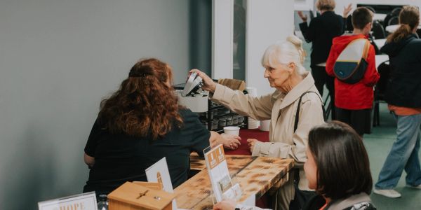Elderly woman gets a cup from a table at an indoor event.
