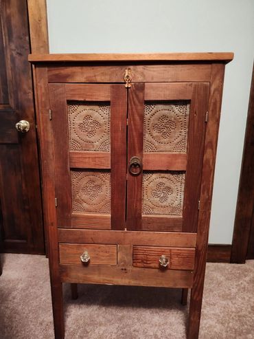 Vintage wooden cabinet with decorative punched tin panels and two drawers.