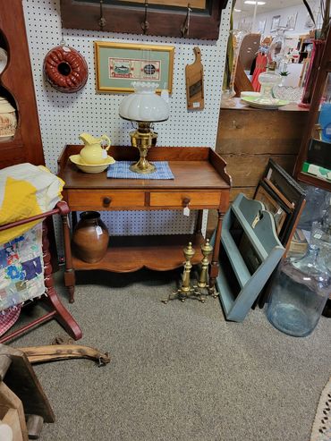 Vintage wooden table with antique lamp, yellow pitcher, and brass andirons in a cozy antique shop.