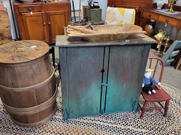 Vintage wooden furniture and decor arranged on a braided rug in an antique shop.