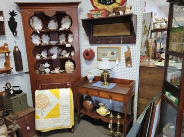 Vintage wooden furniture with antique dishes, quilt, and decorative items in a cozy room.